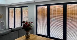blinds for Bi-fold doors with dark grey frame and door blinds partially closed with garden in background.