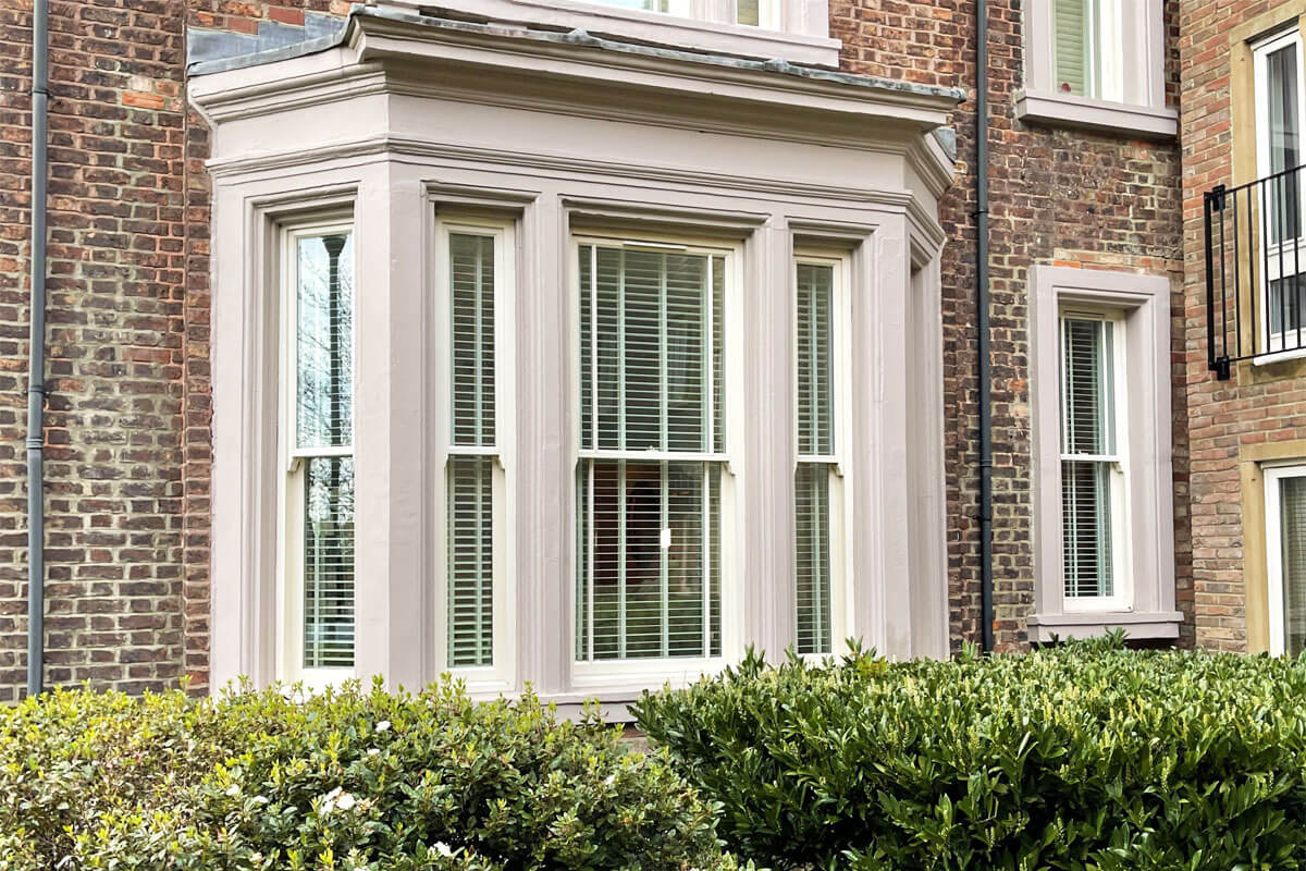 White venetian shutter blinds in large bay window of grand house.