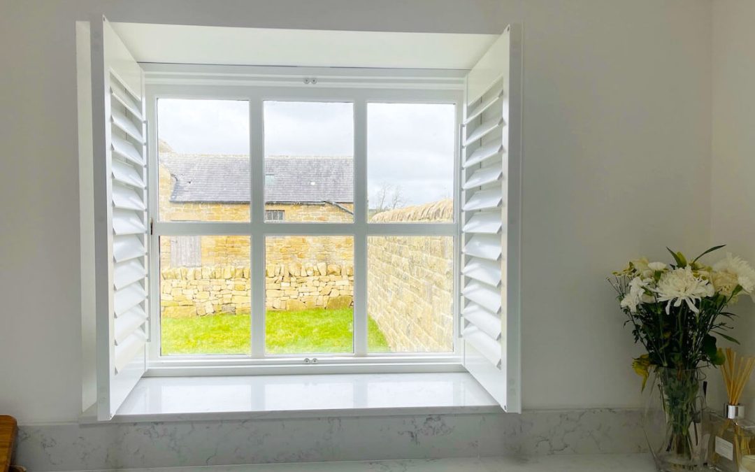 White, wood blinds open showing garden area from kitchen.