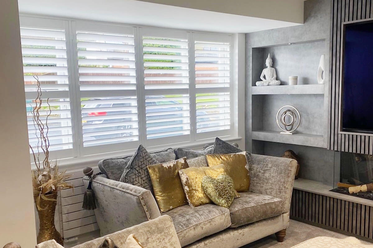 White wooden shutter blinds in modern lounge with brown and gold furniture.