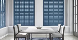 Large blue window shutter in minimalist dining area with grey dining table and seats. Shutters or Blinds