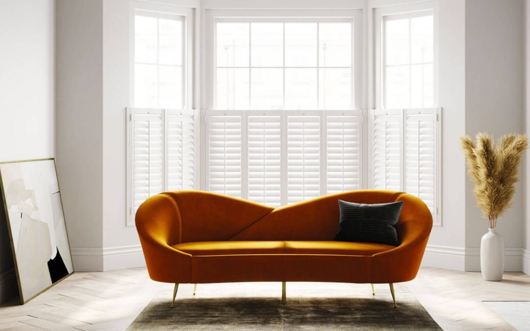 White wooden plantation shutters in large bay windows in very modern, minimalistic lounge area with bright orange chaise lounge in centre of room.
