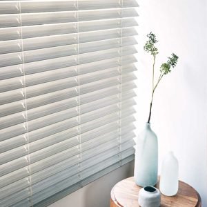 Grey, metal venetian blind in modern reception area with small wooden table.